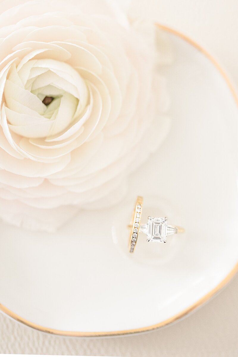 wedding ring sitting on a ring dish next to a ranunculus flower