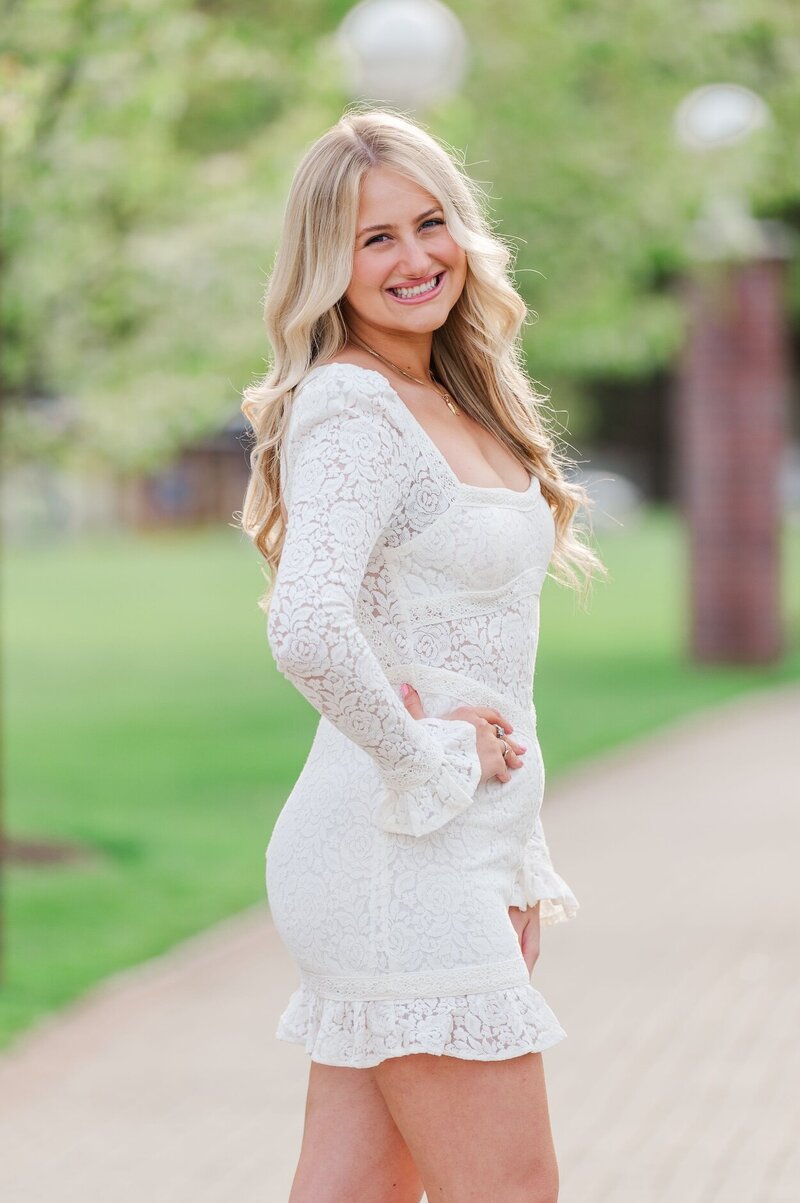 Quinnipiac Nursing School graduate wears a white bodycon dress and smiles. 