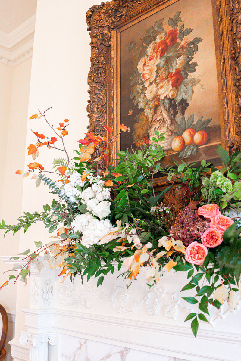 Floral arrangement sitting on mantle with vintage picture frame behind it
