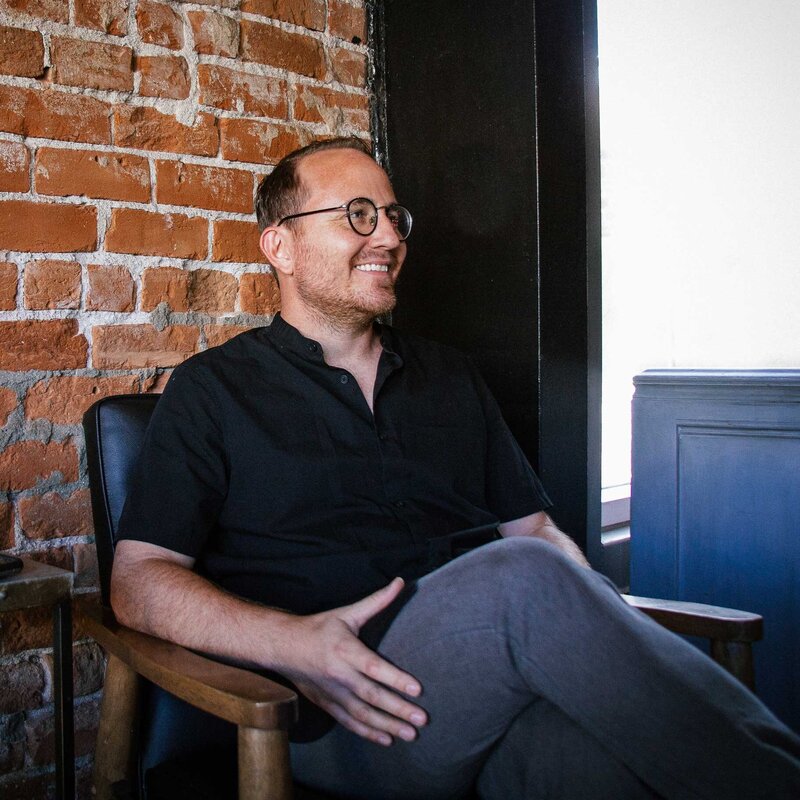 Chris from Self-Made Web Designer sitting on a chair in a coffee shop