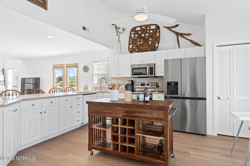 Renovated kitchen with stainless steel appliances, long counter dividing kitchen and living area, and stained wooden island with handcrafted wine storage.