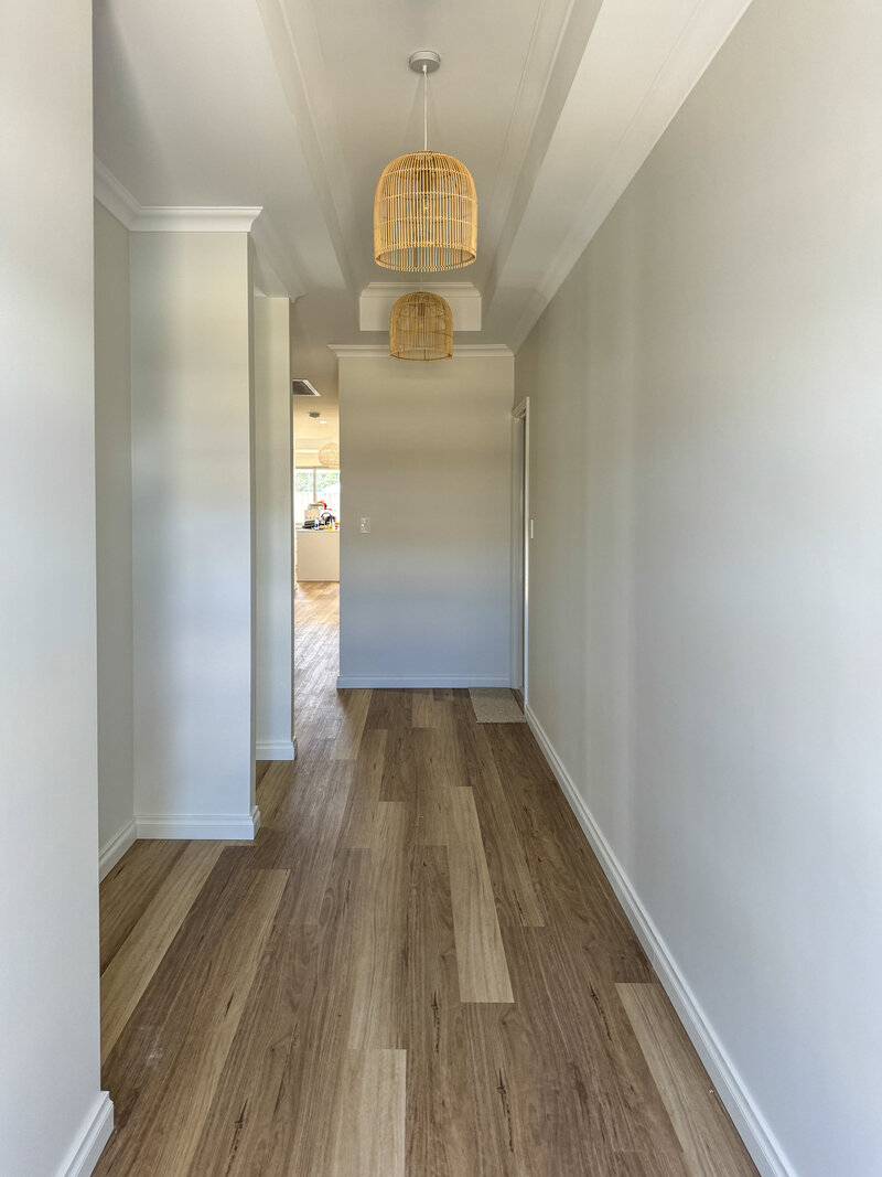 Hallway with off-white grey walls, wooden flooring and two hanging cane light shades.