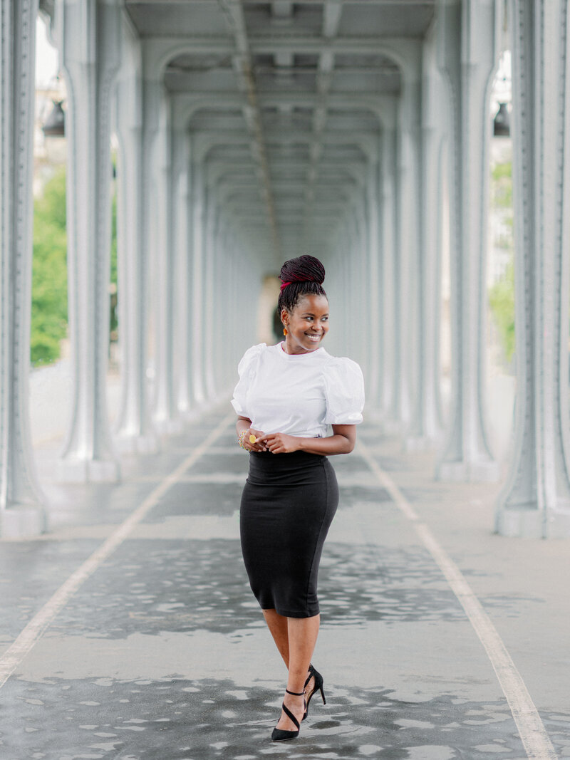a black woman with a white top and black skirt looking off into the distance  under the Bir Hakeim bridge in Paris