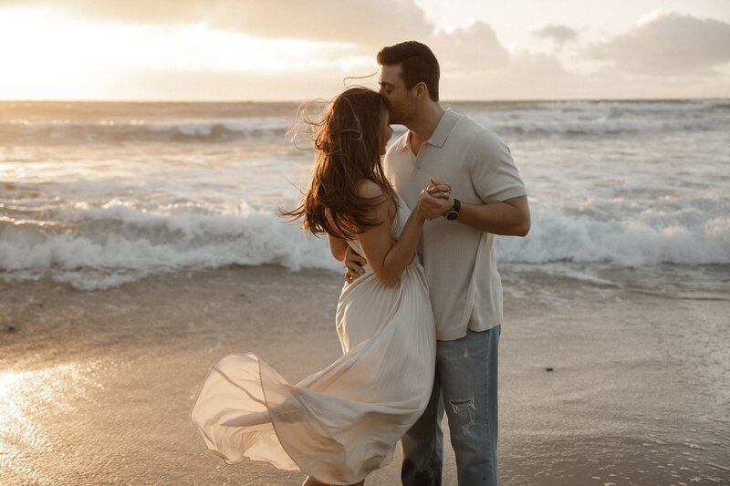 woman gets forehead kiss from fiance during engagement photos on san diego beach