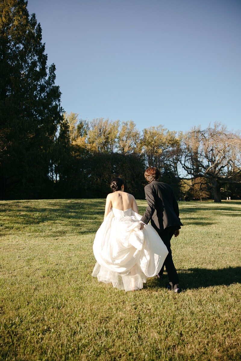 Groom carrying the lower part of the bride's gown while walking towards the field