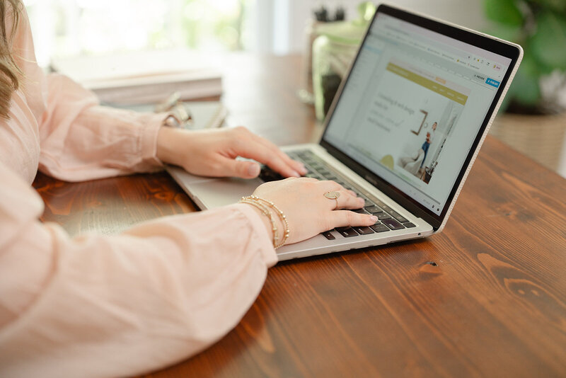 Woman in a pink blouse working on designing a Showit website on her Macbook Pro at a wooden desk