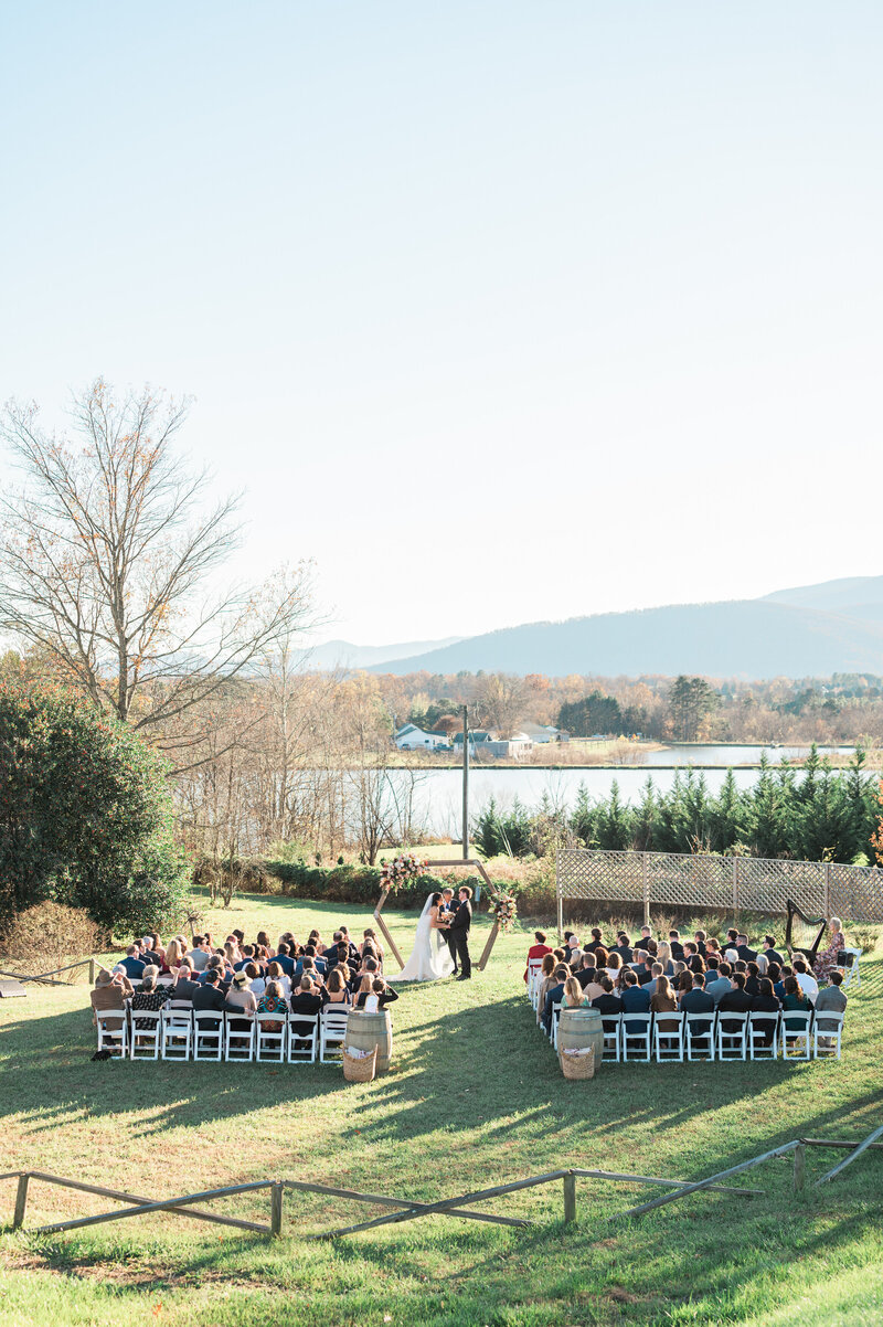 Wide pan view of a couple standing up during their wedding ceremony with guests on either side of a grass aisle