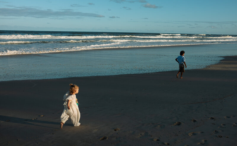 Siblings running wildly on Cabarita Beach at sunset , the waves are visible on the softly lit wide beach