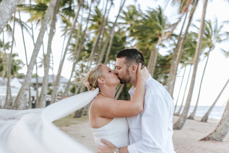 A bride in a blue dress and a groom standing on a balcony overlooking the ocean