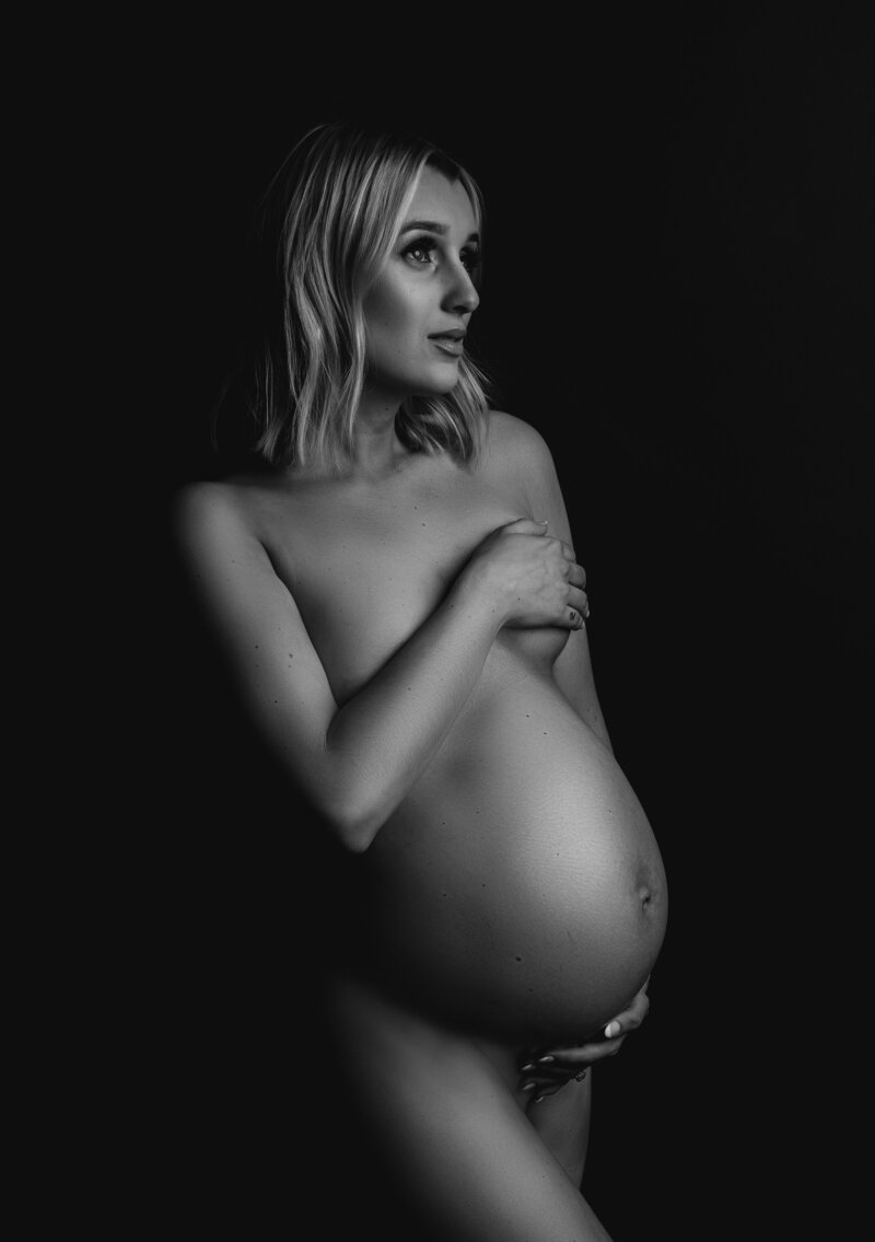 Black and white maternity portrait of nude mother looking off to the side