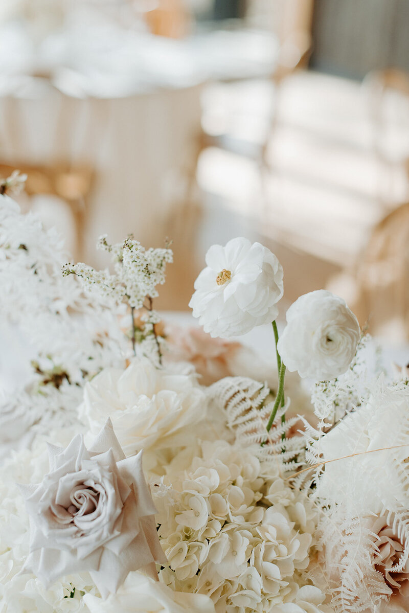 Close-up of reception table with white hydrangea, neutral roses, and bleached fern in lucite vases, styled with candlelight at Jenay and Daniel’s wedding by Summer Robbins Flowers in Central Oregon