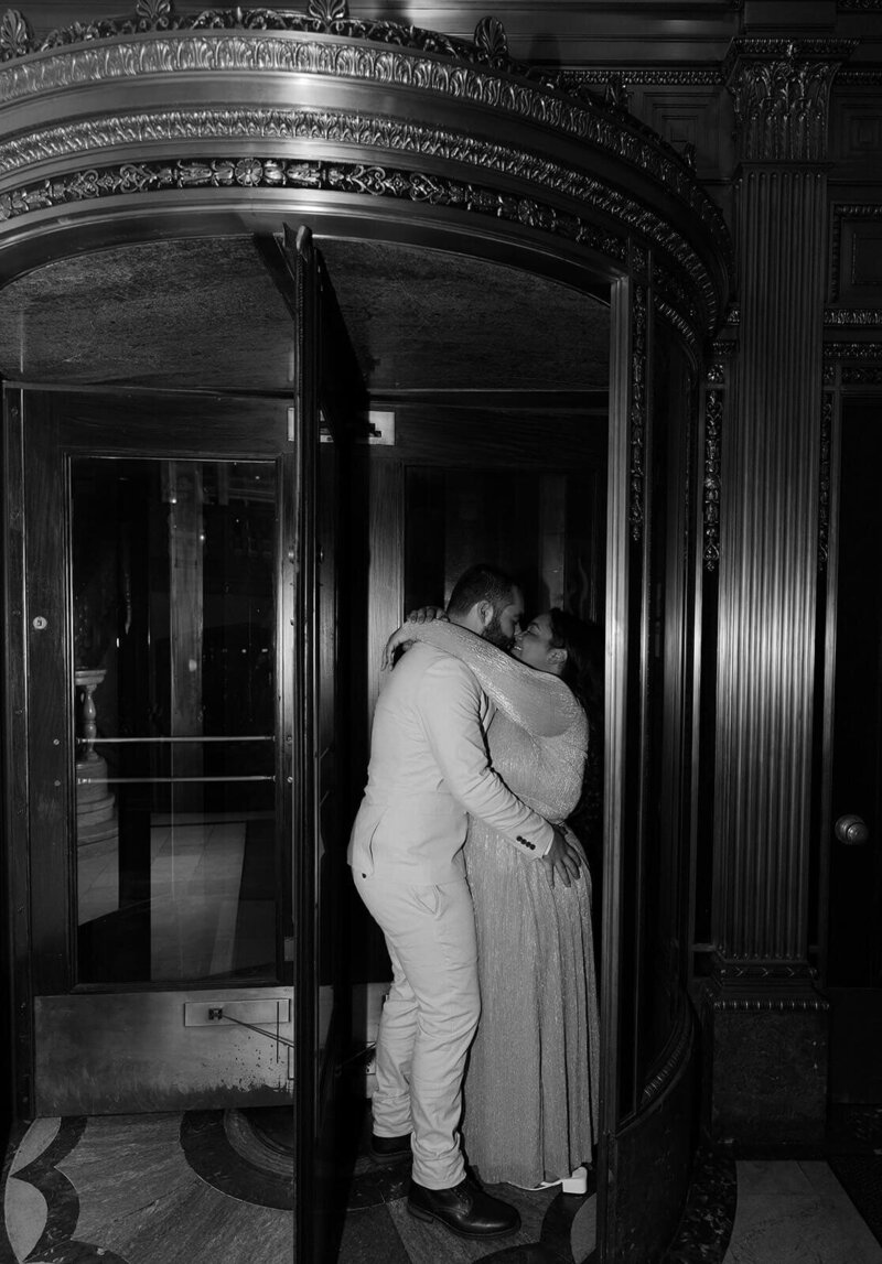 The groom and bride are kissing and hugging in the hotel lobby.