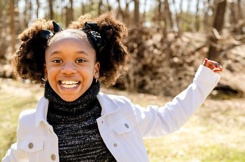 Young black girl laughing as she runs through Morton Arboretum during a family session in Lisle, IL.