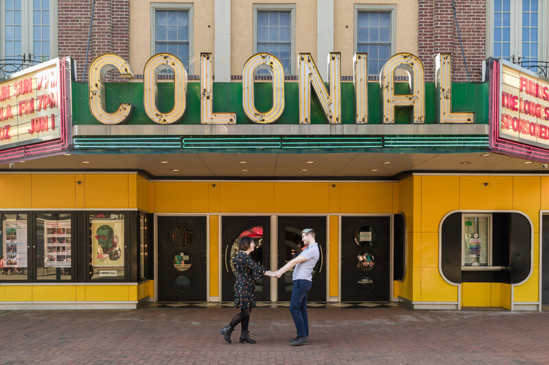 Engaged couple walking joyfully in front of the iconic Colonial Theatre in downtown Phoenixville during their engagement session.