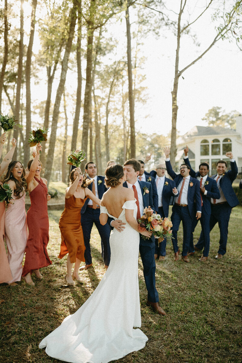 bride and groom kissing while surrounded by wedding party