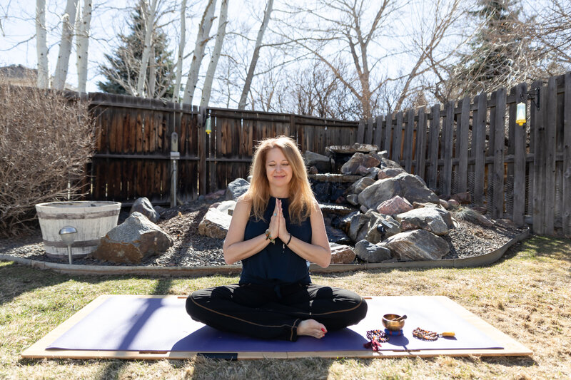 Kundalini yoga teacher Cyndi sitting on her yoga mat. Her hands in prayer position in front of her chest.