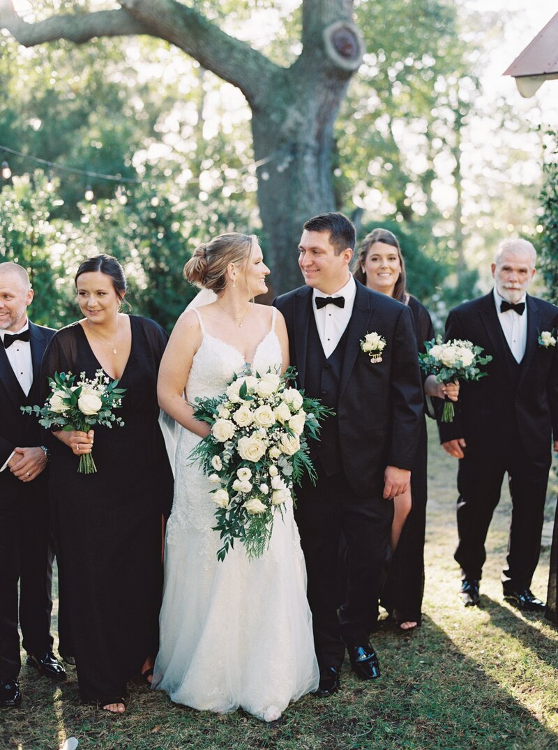 Bride and groom laughing with bridal party walking behind