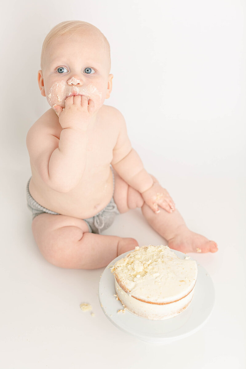 light skinned baby eating a minimalist cake with white frosting in a portland portrait photographer studio