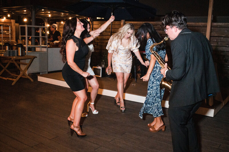 Group of women dancing with a saxaphone player nearby.