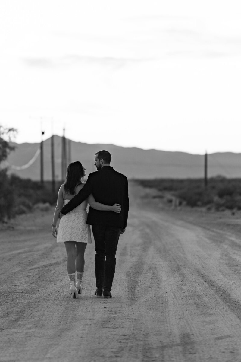 A couple walking with their arms around each other down a dirt road