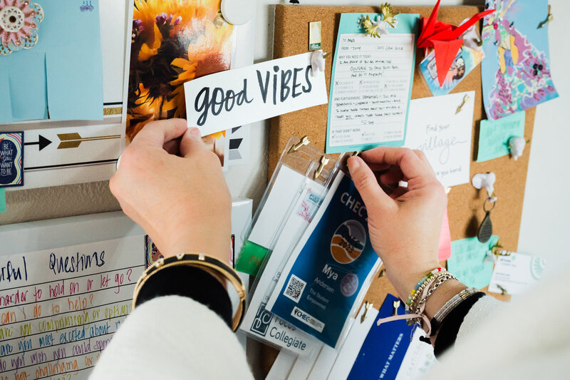 Mya Andersen, an academic life coach, pins a good VIBES note to a corkboard filled with cards and decorations.