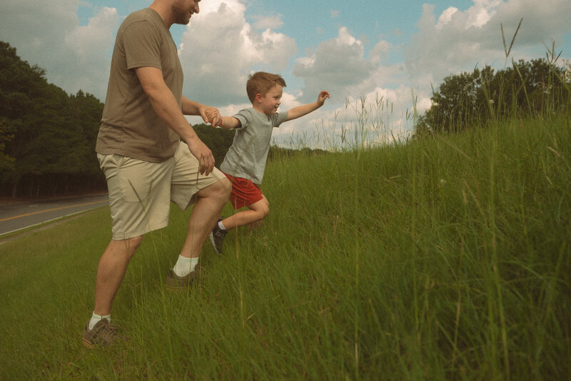 A father and sun run up a grassy hill at Noonday Creek Trail. 