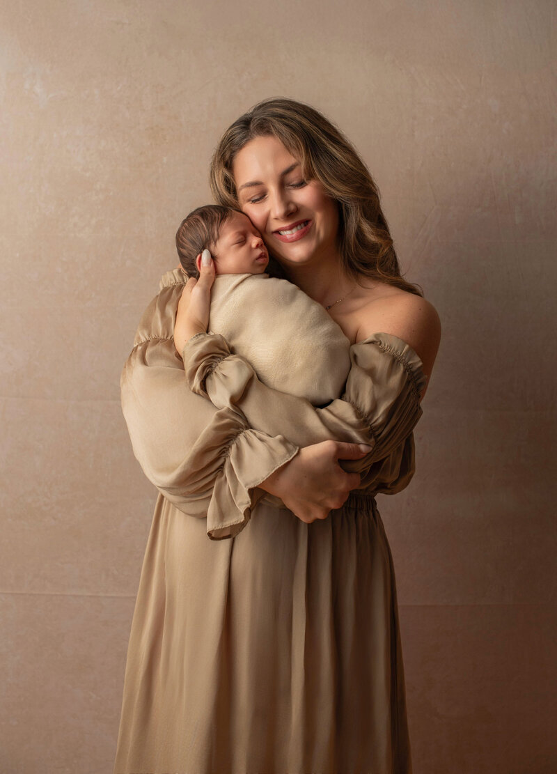 Mom smiling and nestled with newborn daughter for mommy and me photo.