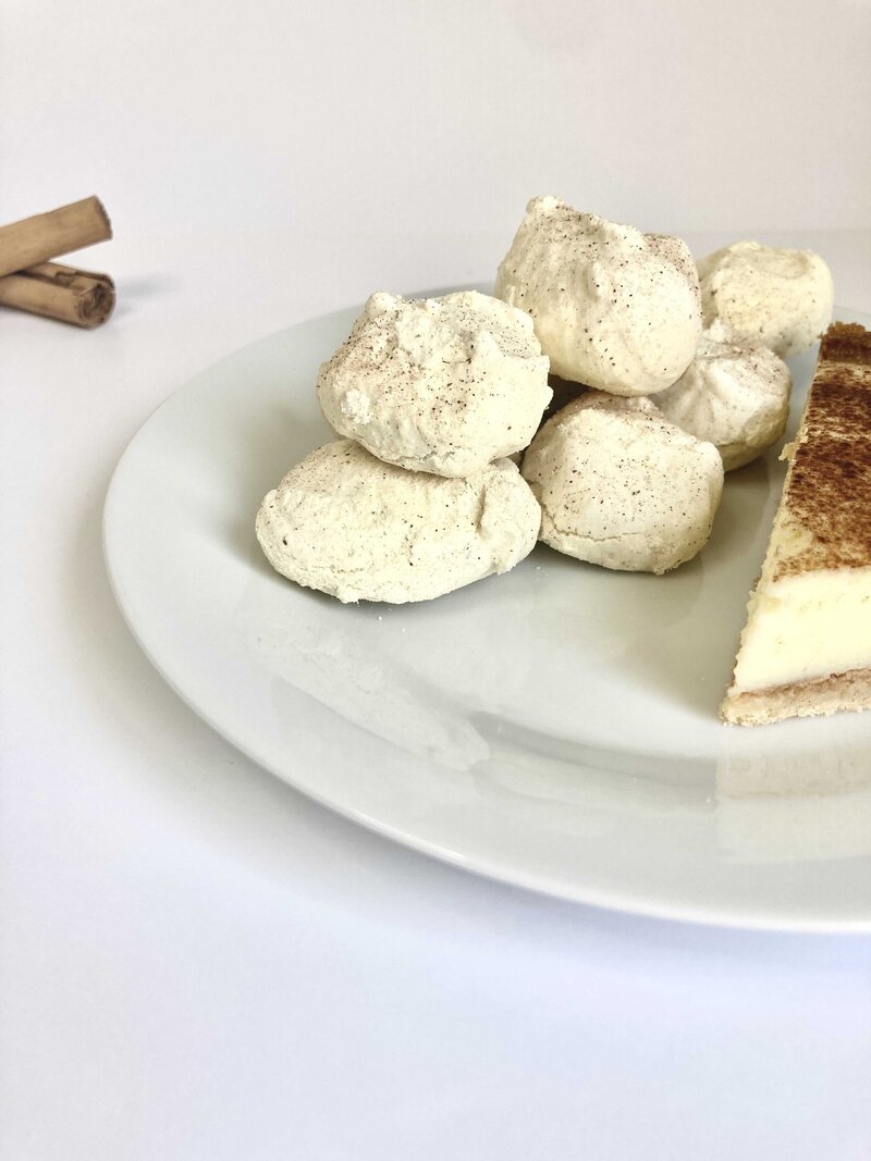 Beige coloured meringue cookies with a slice of milktart on a plate.