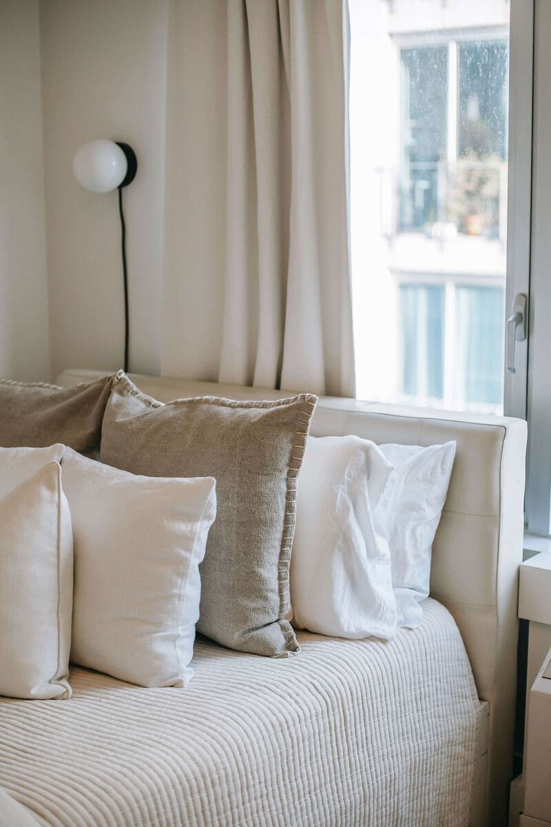 a bed with neutral linens and several pillows