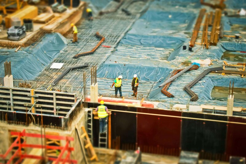 Overhead view of a large construction site with workers in safety vests and helmets inspecting a partially built structure, highlighting industrial progress and teamwork.