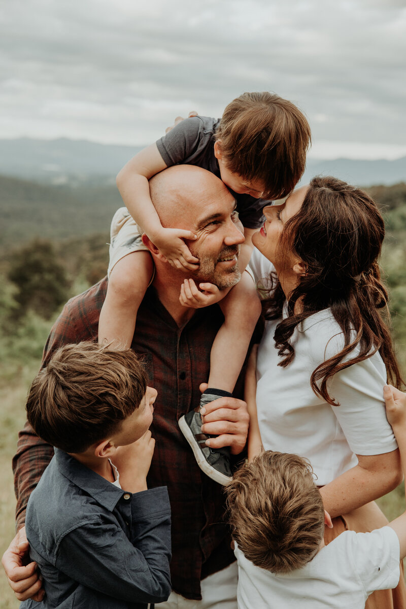 Family cuddle together with young son on dads shoulders