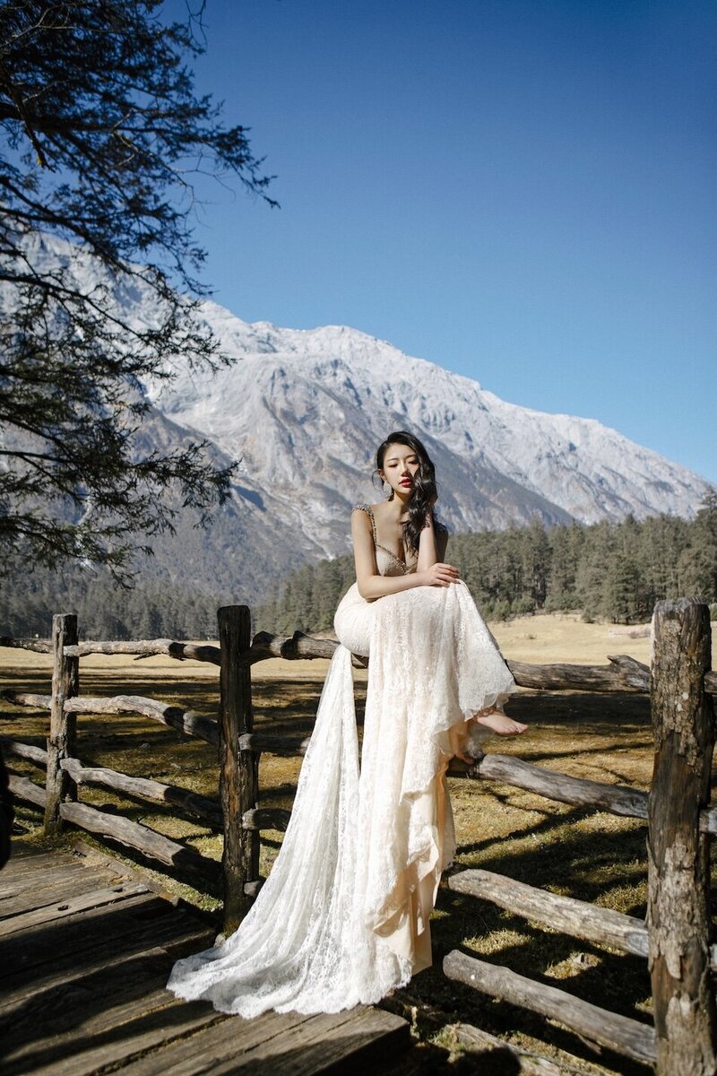 Bride in a couture dress shot in dramatic trees with mountains in the background.