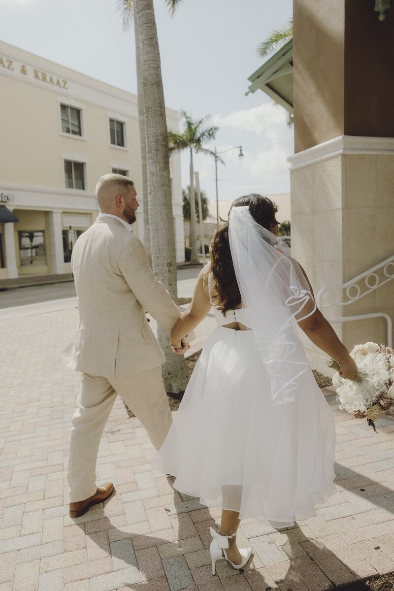 bride and groom hold hands as they walk out of the courthouse