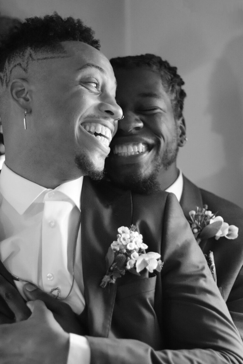 Two Black grooms laughing and embracing