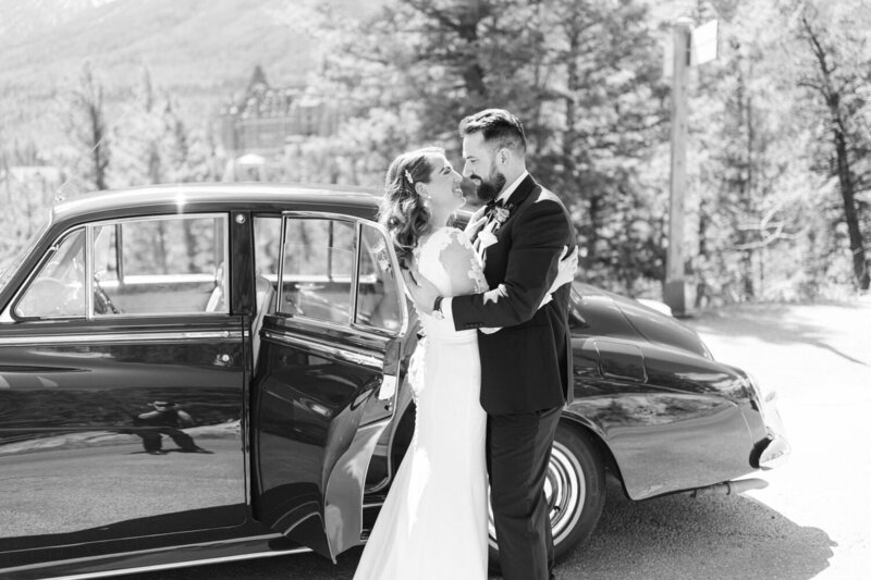 Black and white portrait of a bride and groom looking at each other at Surprise Corner in Banff with the Fairmont Banff Springs Hotel in the background after arriving in a luxury Rolls Royce