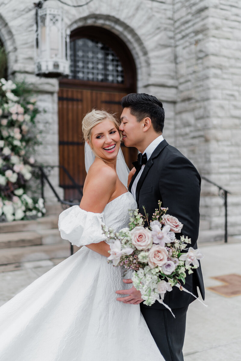 bide and groom hugging as groom leans in to give bride a kiss on the cheek