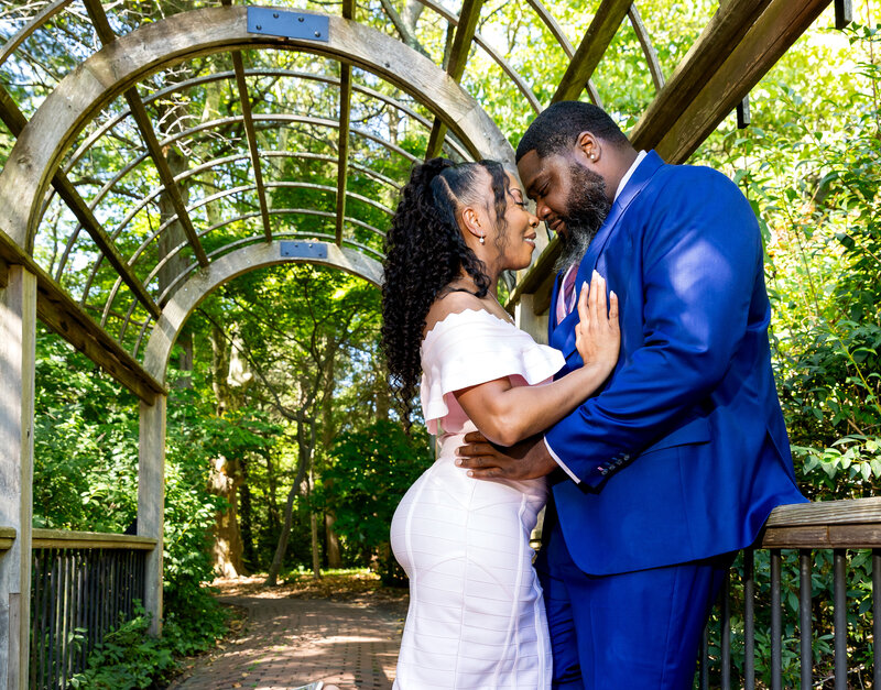 A black young couple taking engagement photos. The couple are wearing blue and pink. The couple is in garden in Hamilton, NJ.