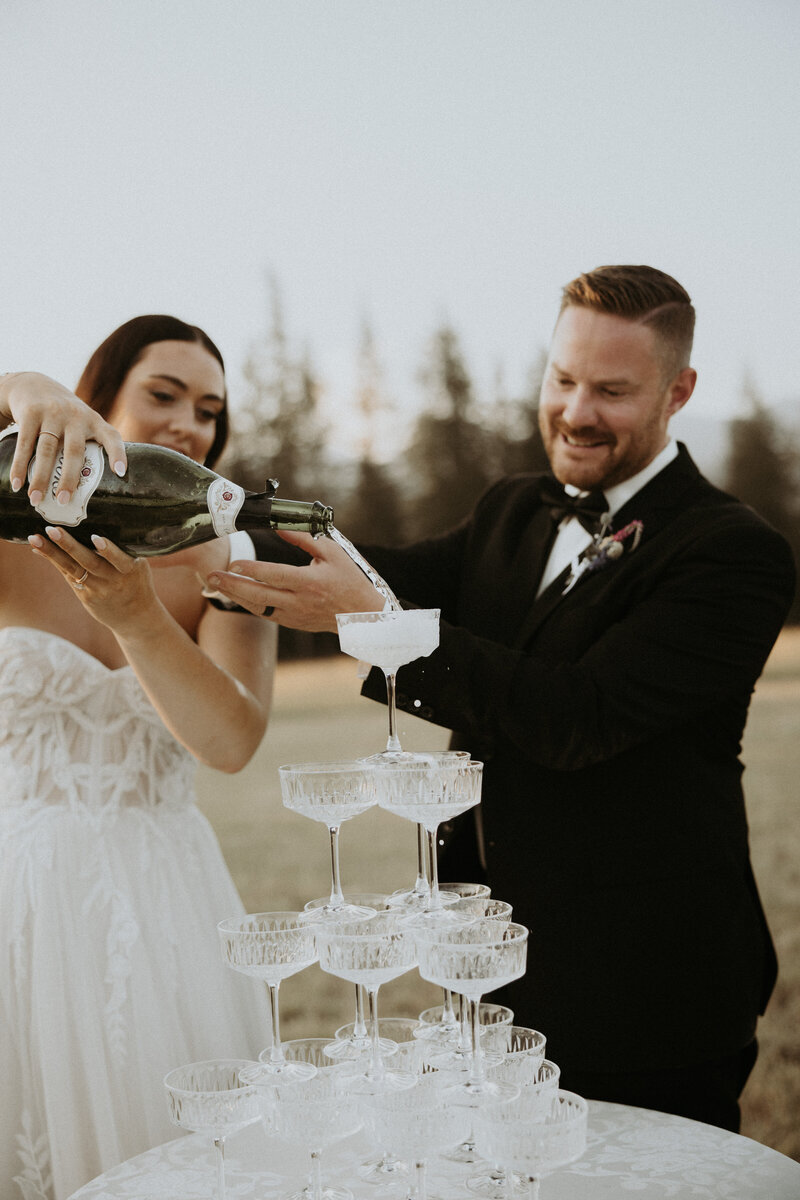 photo of bride and groom pouring champagne in coupes at their traditional montana wedding 