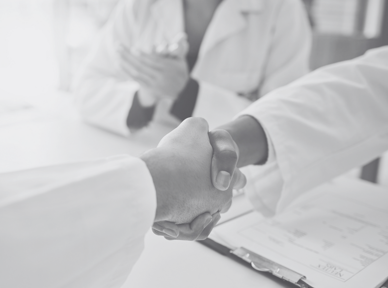 Two individuals in lab coats shake hands over a clipboard with medical forms, symbolizing collaboration or agreement.
