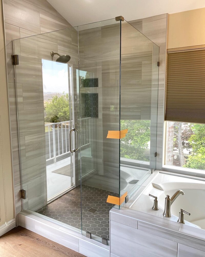 Large Tiled Shower with Large grey and white striped tiles to look like faux wood. There is a new shower enclosure made of glass that has brushed nickel hardware next to a tiled tub.