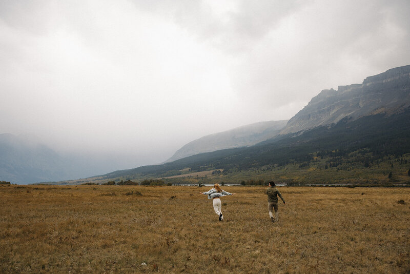 couple running through a field in glacier national park