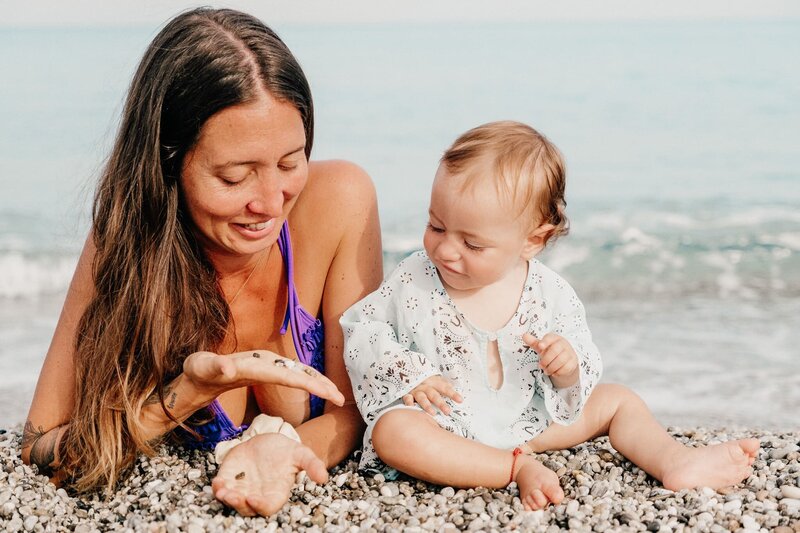 Mother and baby playing together on a pebble beach, embracing mindful connection and nature.