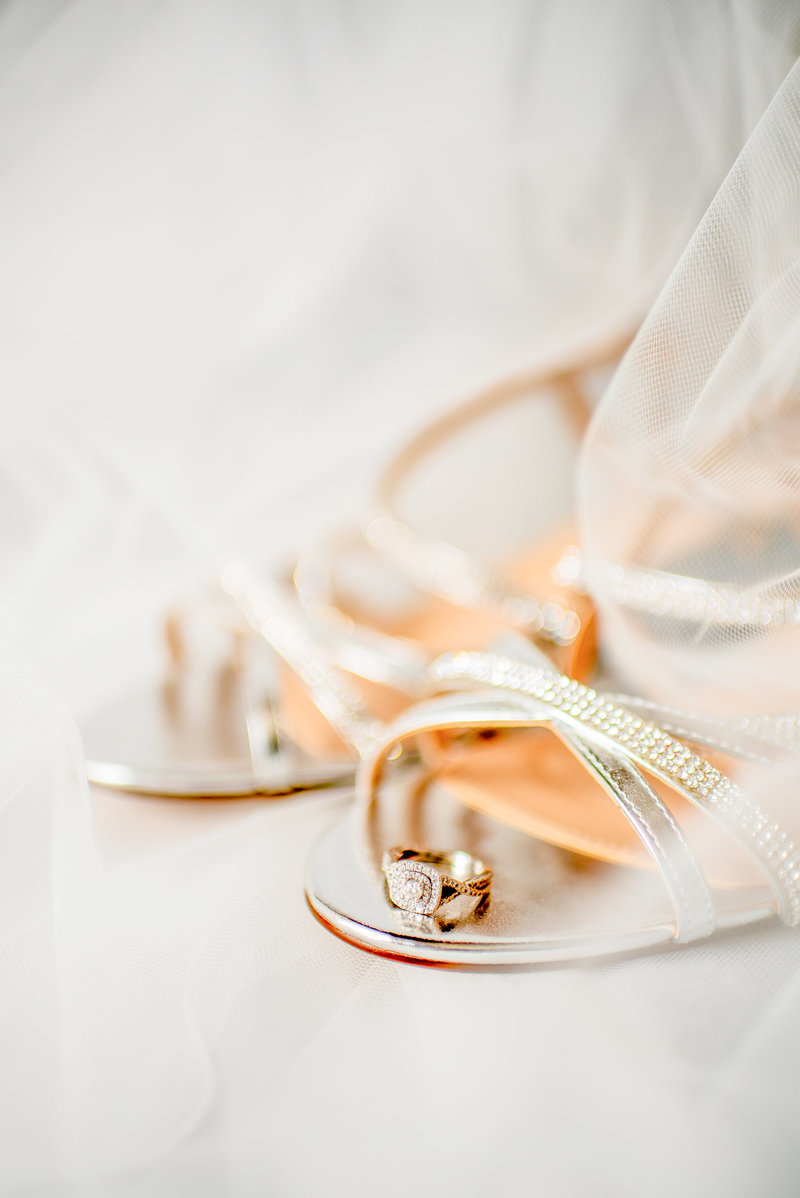A yellow gold band diamond ring sits on the toe of a bride's wedding shoe