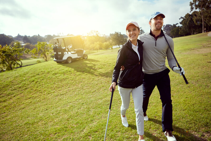 Woman golfing next to a beautiful scenic ocean with her golf caddy standing in the background