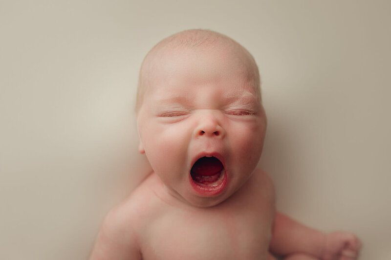 a newborn boy yawning on a white backdrop