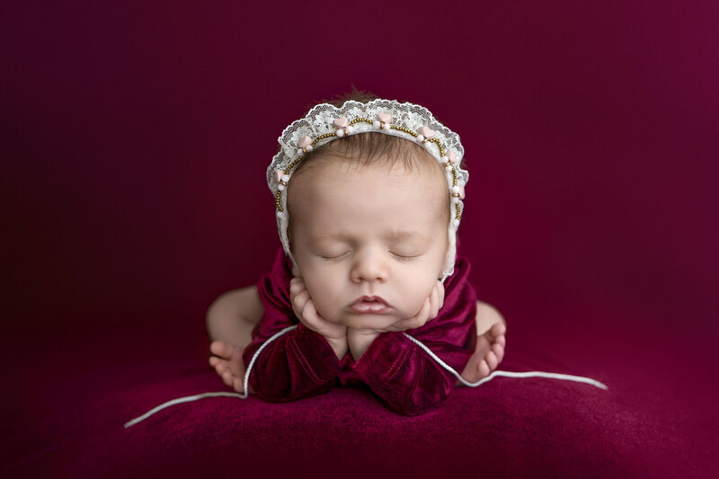 Tacoma newborn is posed with hands under chin and toes sticking out by elbows. Baby is wearing headband with hearts and lace.