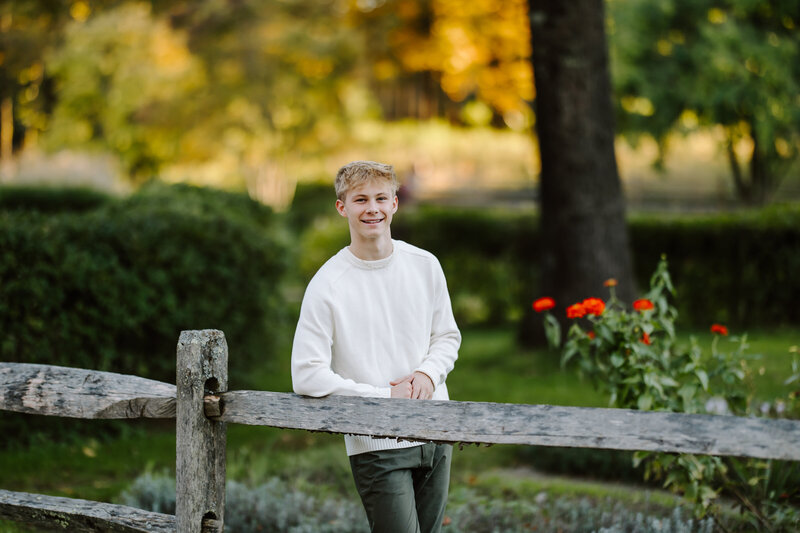 Senior boy smiles and leans on fence during his fall senior session in Hollis, New Hampshire