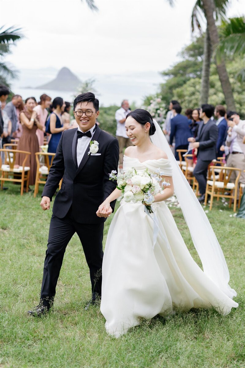 A newlywed couple holding hands and walking back up the aisle 
