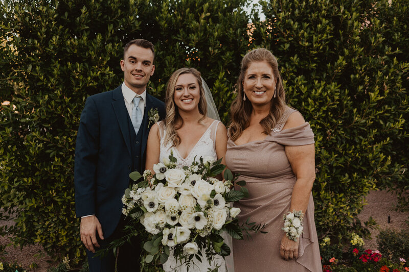 A bride and groom smiling with their mother.