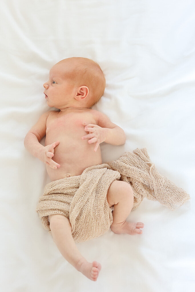 Newborn lying on a vintage quilt, surrounded by warm earthy tones and soft textures. A nostalgic moment by Sophie Louise.